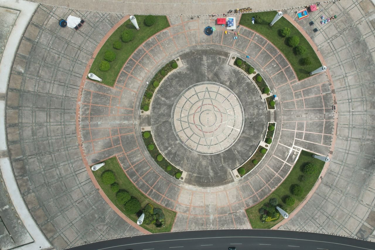 Overhead image of a geometrically designed plaza surrounded by greenery, captured in daylight.